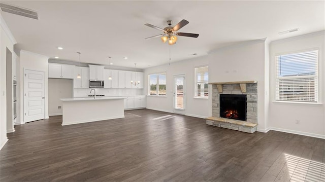 unfurnished living room featuring a fireplace, dark wood-type flooring, ornamental molding, and ceiling fan