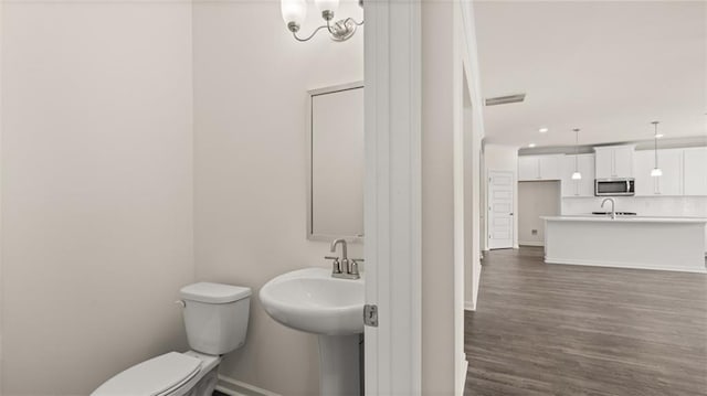 bathroom with wood-type flooring, an inviting chandelier, and toilet