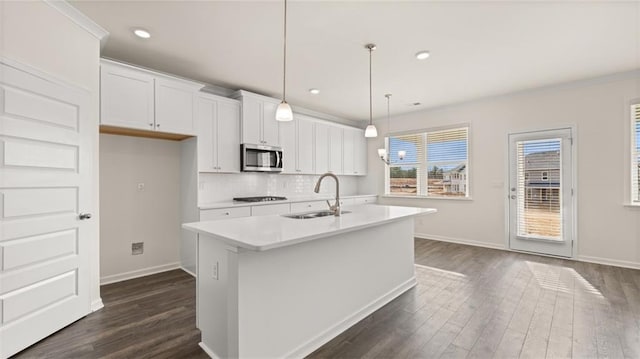 kitchen featuring sink, hanging light fixtures, a center island with sink, white cabinets, and backsplash