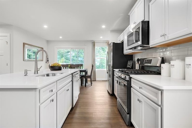 kitchen with dark wood finished floors, an island with sink, a sink, decorative backsplash, and stainless steel appliances