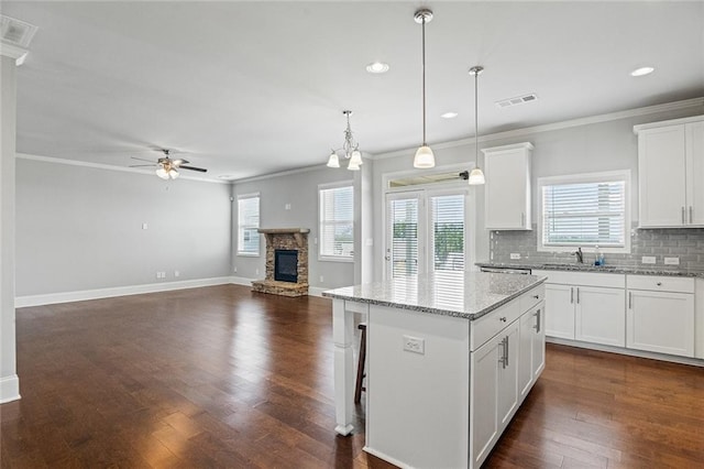 kitchen featuring ceiling fan, a stone fireplace, dark wood-style flooring, a kitchen island, and decorative backsplash