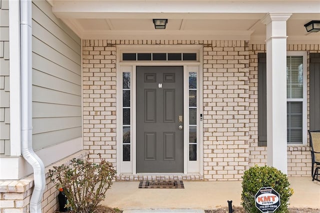 doorway to property with a porch and brick siding