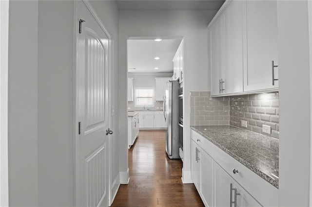 kitchen featuring light stone counters, dark wood-style flooring, freestanding refrigerator, and white cabinetry