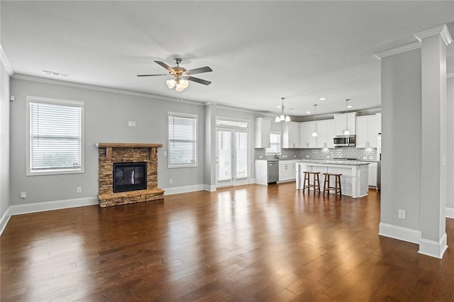 unfurnished living room featuring visible vents, baseboards, a ceiling fan, ornamental molding, and dark wood-style floors