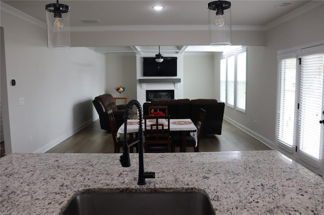 kitchen with wood-type flooring, hanging light fixtures, a brick fireplace, light stone counters, and crown molding