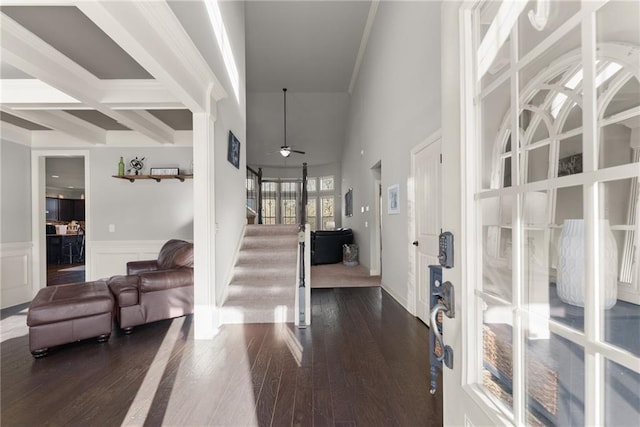 foyer featuring a wainscoted wall, beam ceiling, a ceiling fan, stairs, and dark wood-style flooring