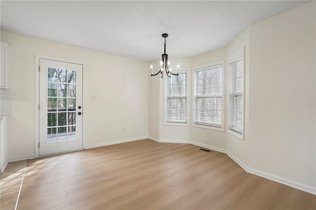 unfurnished dining area with a chandelier, a textured ceiling, baseboards, and light wood-style floors