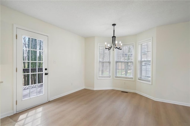 unfurnished dining area featuring visible vents, baseboards, light wood-type flooring, a notable chandelier, and a textured ceiling