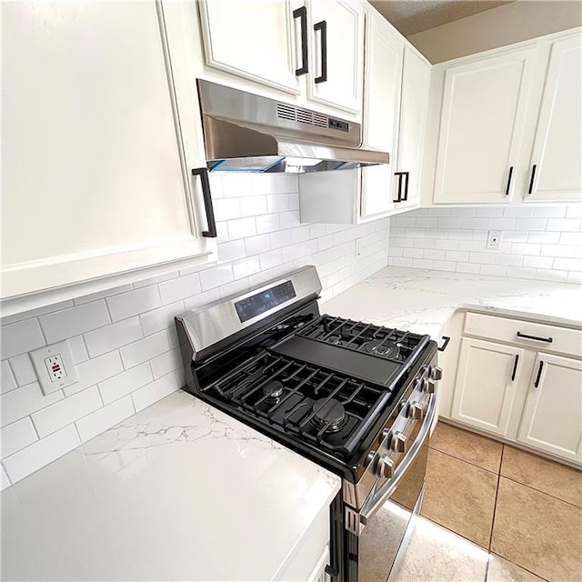 kitchen featuring backsplash, light stone countertops, under cabinet range hood, white cabinets, and gas stove