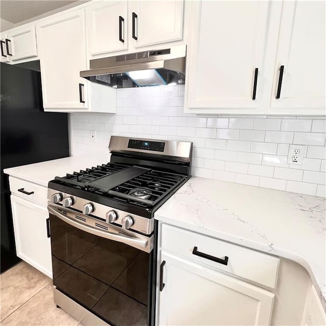 kitchen featuring backsplash, stainless steel range with gas cooktop, under cabinet range hood, light tile patterned floors, and white cabinetry