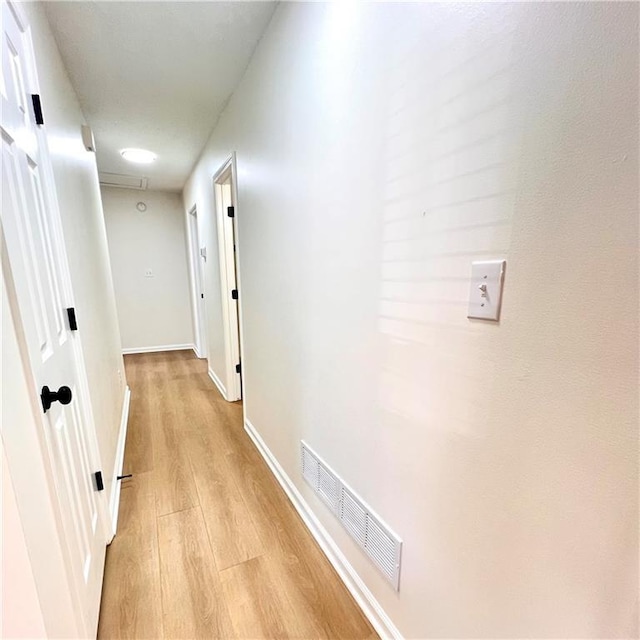 hallway with baseboards, visible vents, and light wood-type flooring