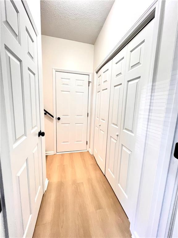 hall featuring light wood-type flooring and a textured ceiling