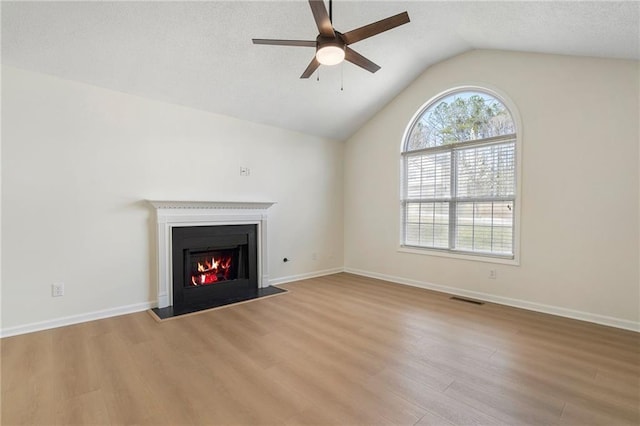 unfurnished living room with visible vents, a lit fireplace, vaulted ceiling, wood finished floors, and a ceiling fan