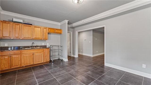 kitchen featuring dark tile patterned flooring, ornamental molding, a sink, dark countertops, and baseboards