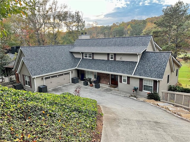 traditional-style house featuring a chimney, roof with shingles, concrete driveway, and an attached garage