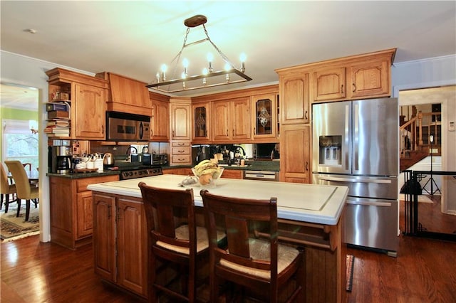 kitchen featuring a kitchen island, dark wood-style floors, stainless steel appliances, brown cabinetry, and crown molding