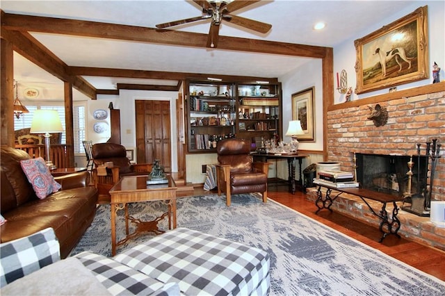 living area with beamed ceiling, a wainscoted wall, wood finished floors, a brick fireplace, and ceiling fan