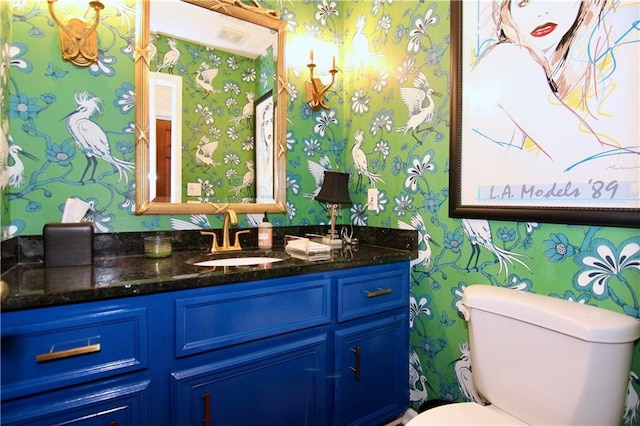 bathroom with toilet, vanity, and wallpapered walls