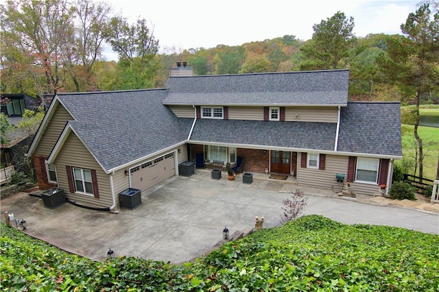 view of front of house featuring an attached garage, a shingled roof, entry steps, a chimney, and driveway