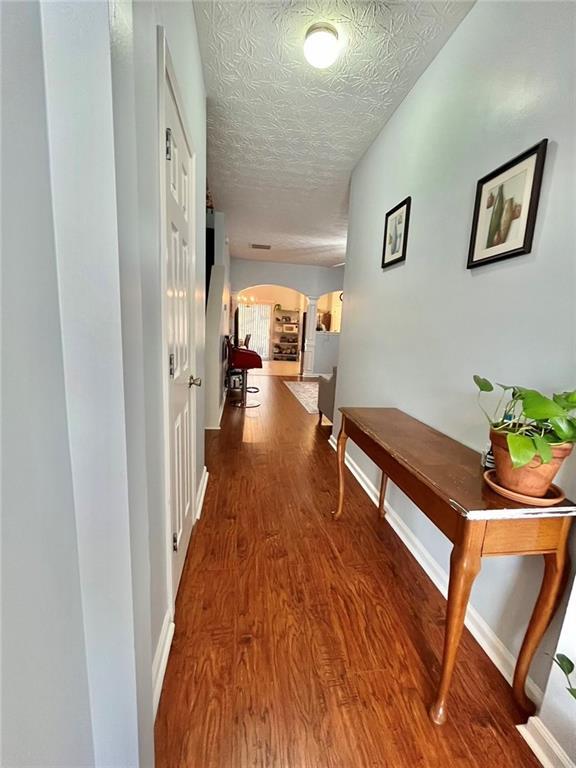 hall with baseboards, a textured ceiling, arched walkways, and wood finished floors