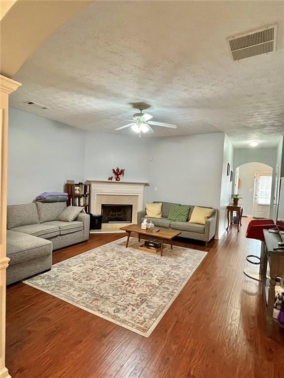 living area featuring arched walkways, a fireplace, visible vents, dark wood-type flooring, and a textured ceiling