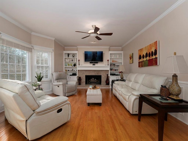 living room featuring a tiled fireplace, crown molding, light hardwood / wood-style floors, and ceiling fan