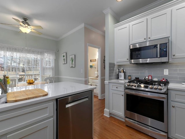 kitchen with light hardwood / wood-style flooring, white cabinetry, stainless steel appliances, ornamental molding, and decorative backsplash