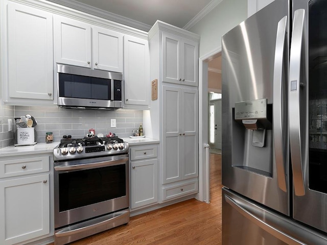 kitchen featuring ornamental molding, white cabinets, stainless steel appliances, light hardwood / wood-style floors, and backsplash