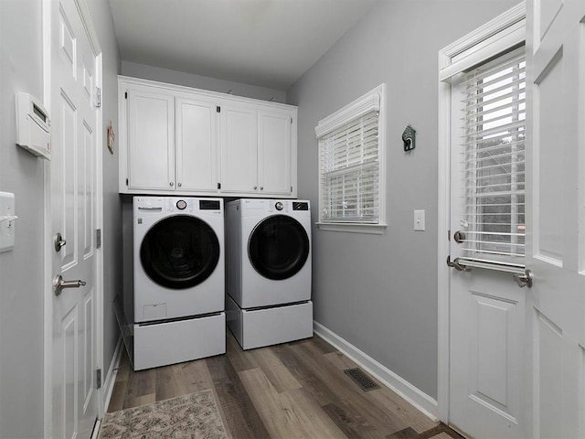 laundry area featuring cabinets, a healthy amount of sunlight, dark wood-type flooring, and independent washer and dryer