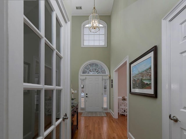 entrance foyer with a towering ceiling, ornamental molding, light wood-type flooring, and a notable chandelier