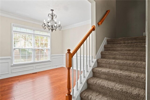 stairs with ornamental molding, an inviting chandelier, and hardwood / wood-style flooring