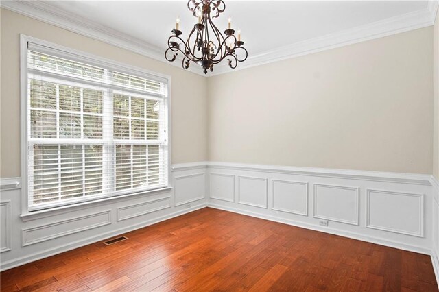 empty room with ornamental molding, an inviting chandelier, and hardwood / wood-style floors