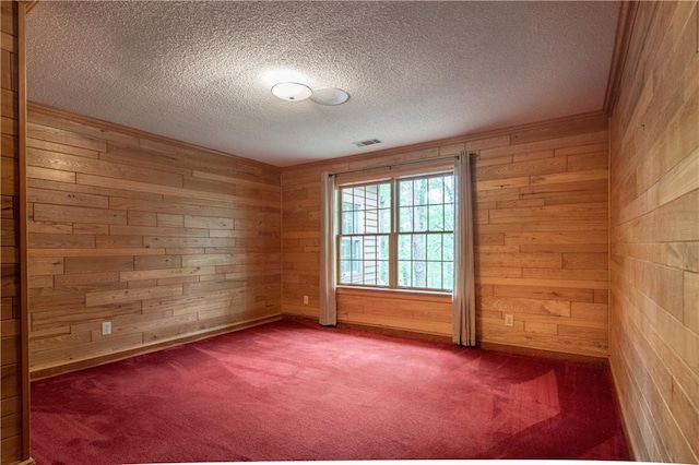 carpeted spare room featuring wooden walls and a textured ceiling