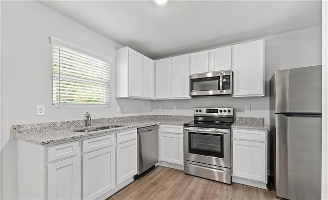 kitchen with appliances with stainless steel finishes, light stone countertops, white cabinets, light hardwood / wood-style floors, and sink