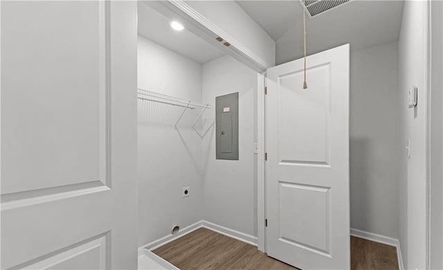 clothes washing area with electric panel, electric dryer hookup, and wood-type flooring