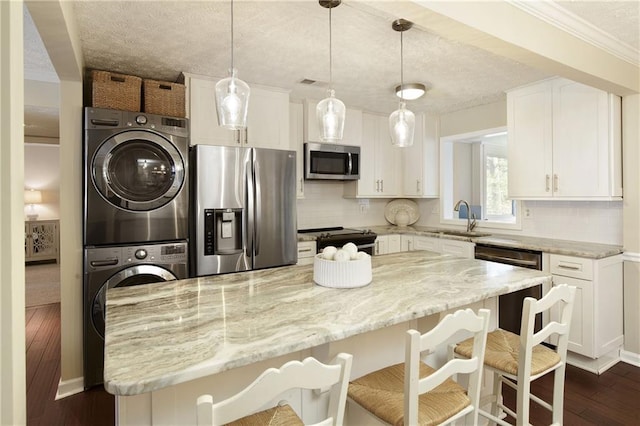 kitchen featuring stacked washer / drying machine, backsplash, appliances with stainless steel finishes, white cabinetry, and a sink