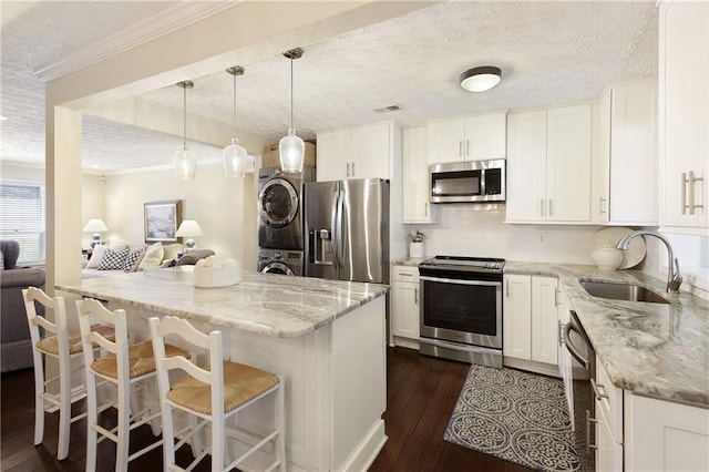 kitchen with stacked washer and clothes dryer, stainless steel appliances, dark wood-type flooring, white cabinets, and a sink