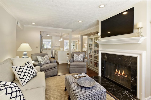 living area with a textured ceiling, a notable chandelier, a premium fireplace, visible vents, and ornamental molding