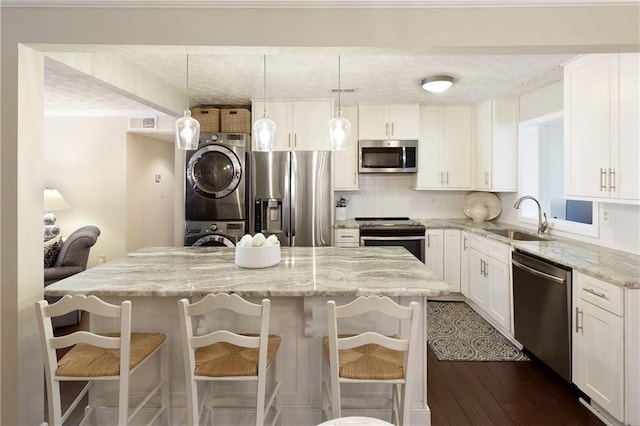 kitchen with white cabinets, decorative backsplash, appliances with stainless steel finishes, stacked washing maching and dryer, and a sink