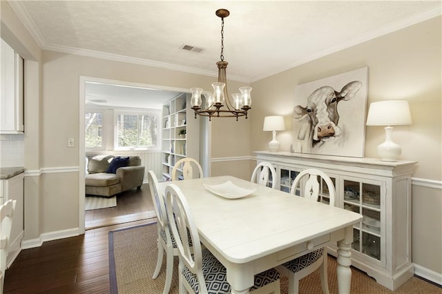 dining space with visible vents, dark wood-type flooring, ornamental molding, a chandelier, and baseboards