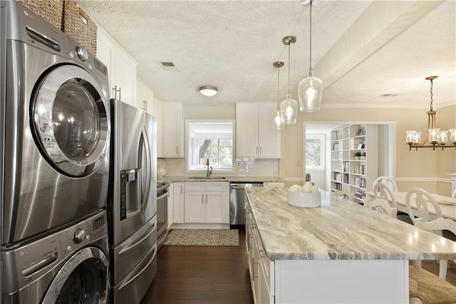 kitchen featuring a sink, stacked washer / drying machine, appliances with stainless steel finishes, a center island, and tasteful backsplash