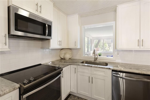 kitchen featuring light stone counters, appliances with stainless steel finishes, a sink, and white cabinetry