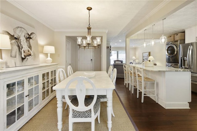 dining area featuring stacked washer and dryer, a notable chandelier, ornamental molding, and dark wood-style flooring