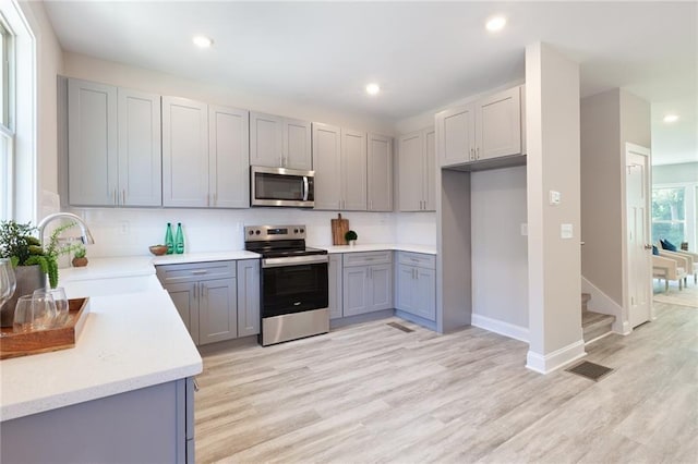 3810 Jack Vernon Cir, Powder Springs, GA 30127 - kitchen featuring appliances with stainless steel finishes, a sink, gray cabinetry, backsplash, and light wood-style floors