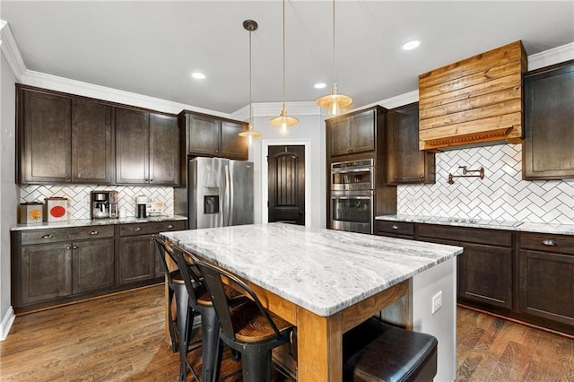 kitchen with dark wood-style floors, light stone countertops, ornamental molding, dark brown cabinets, and appliances with stainless steel finishes