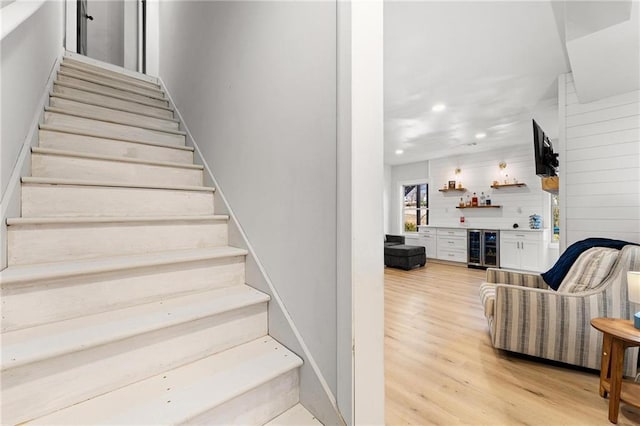 stairs featuring wood finished floors, wine cooler, a dry bar, and recessed lighting