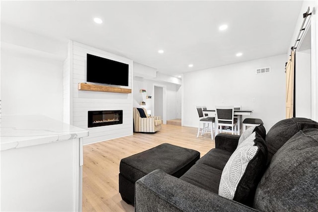 living area featuring a barn door, a fireplace, visible vents, and light wood-type flooring