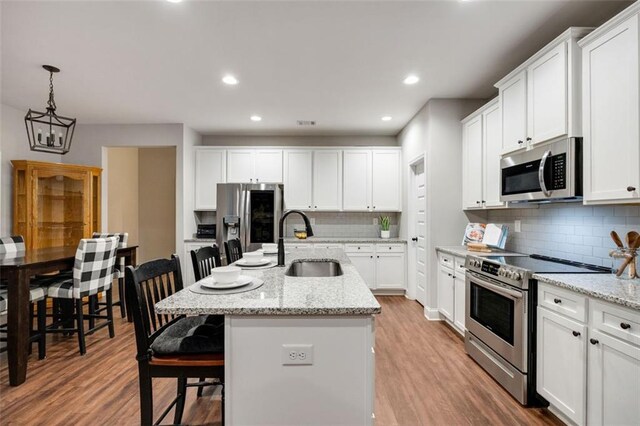 kitchen with a breakfast bar, stainless steel appliances, white cabinetry, a sink, and light wood-type flooring