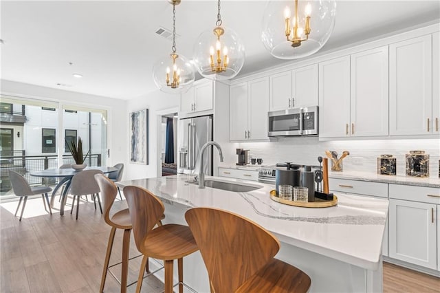 kitchen featuring sink, stainless steel appliances, a center island with sink, and light wood-type flooring