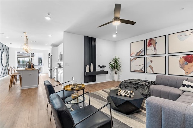 living room with ceiling fan with notable chandelier and light hardwood / wood-style flooring